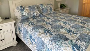 Une chambre à coucher avec un lit blanc, une literie à motifs floraux, une table de chevet avec une lampe et une armoire.