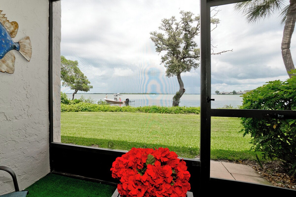 Una habitación con vista a un lago, un bote y un arreglo floral rojo.