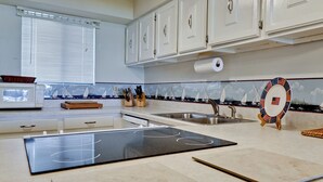 Una cocina moderna con armarios blancos, microondas, lavamanos y un salpicadero decorativo con barcos de vela.