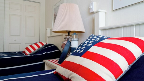 Une chambre avec deux lits, chacun orné d’un oreiller décoré du motif du drapeau américain.