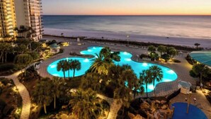 A resort with a large pool, palm trees, and a view of the ocean at sunset. - Edgewater Windward B-105 (Panama City Beach)