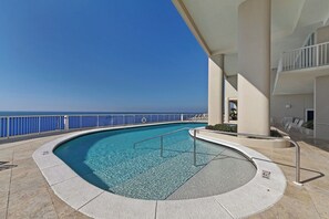 A pool with a clear view of the ocean, surrounded by a white railing and a covered area with lounge chairs. - Palazzo 1604 (Panama City Beach)
