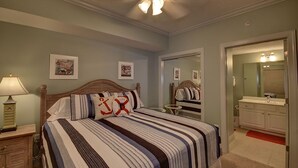 A bedroom with a bed, a nightstand, a dresser, a ceiling fan, and a bathroom with a mirror and sink. - Palazzo 1604 (Panama City Beach)