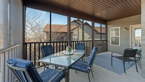 A covered patio with a glass table and blue cushioned chairs, overlooking a residential area.