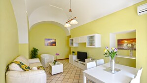 A living room with a sofa, a coffee table, a TV, and a dining table with chairs. There is a plant on the coffee table and a painting on the wall. - Palazzo Rocco - Villa Red Moon in Love - 1 Room - 1 bath - 4 person - Sea 500 mt (Praiano)