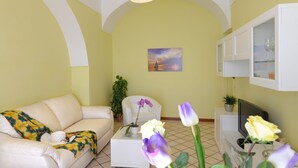 A living room with a sofa, coffee table, and a TV. There is a painting on the wall and a plant on the coffee table. - Palazzo Rocco - Villa Red Moon in Love - 1 Room - 1 bath - 4 person - Sea 500 mt (Praiano)