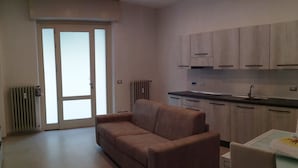 Una sala de estar moderna con un sofá, una mesa de comedor con sillas, y una zona de cocina con armarios y un lavamanos.