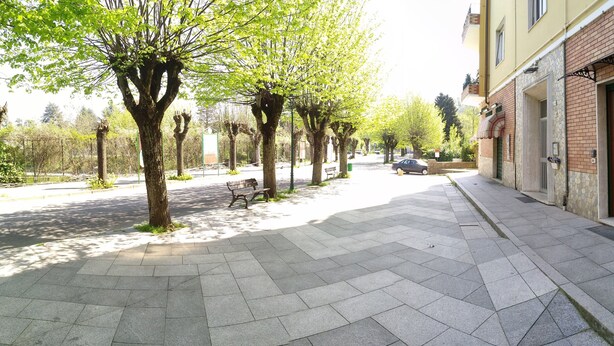 Un camino pavimentado con bancos, árboles y un edificio de fachada de piedra con una puerta marcada '12'.