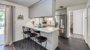 A modern kitchen with a central island, bar stools, stainless steel appliances, and a view of the outdoors.