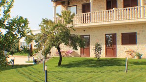 Un bâtiment en pierre de deux étages, doté d’un balcon, d’une pelouse et d’un arbre.
