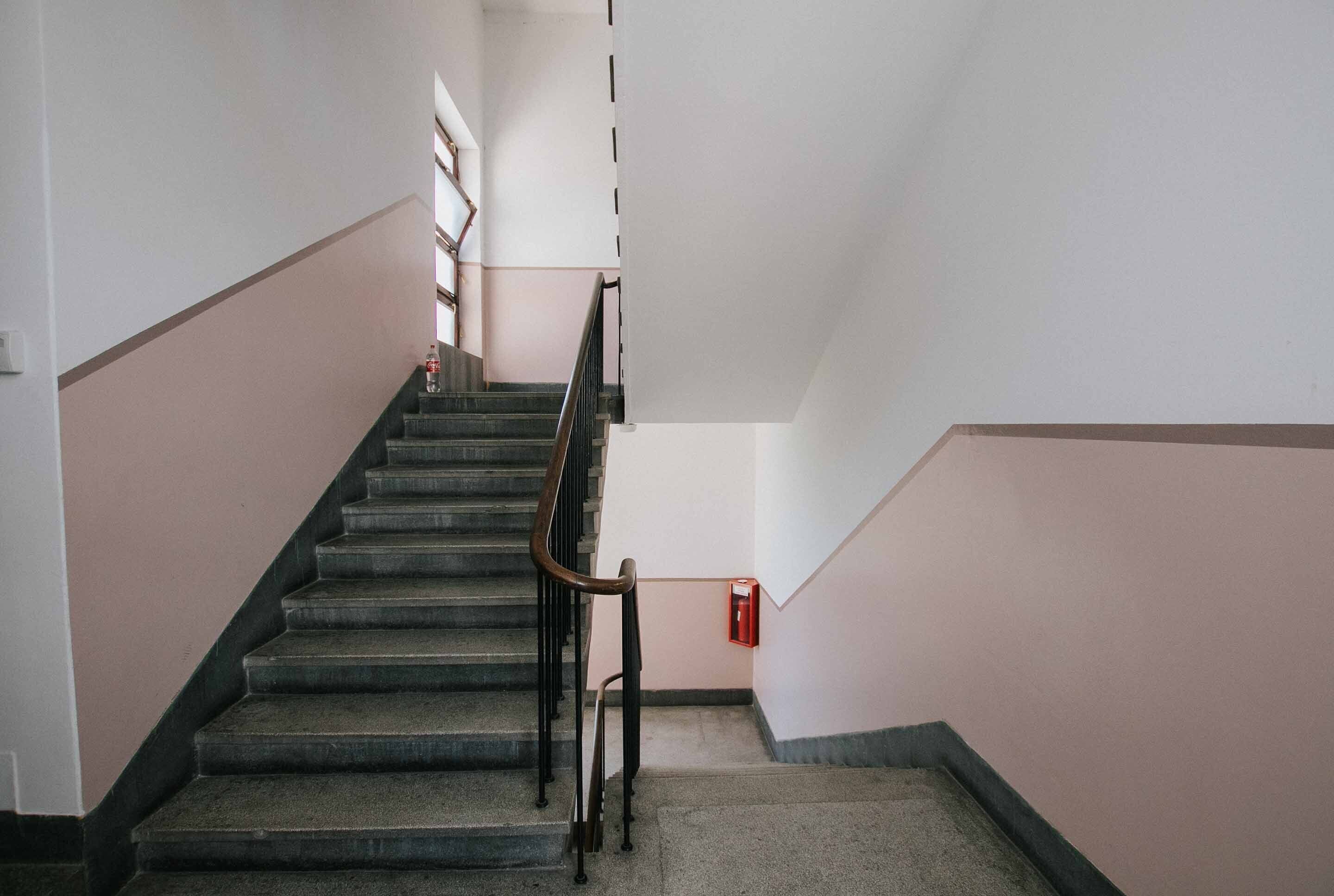 Uma escada com corrimão, um extintor de incêndio fixado na parede e um interruptor de luz na parede.