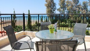 Ein Balkon mit Glastisch, zwei Stühlen und einem Blumentopf.