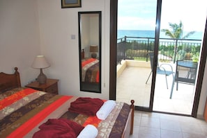 Hotelkamer met een bed, nachtkastje, lamp, spiegel en een balkon met uitzicht op de oceaan.