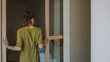 Una persona con un vestido verde de pie frente a una puerta corrediza de vidrio.