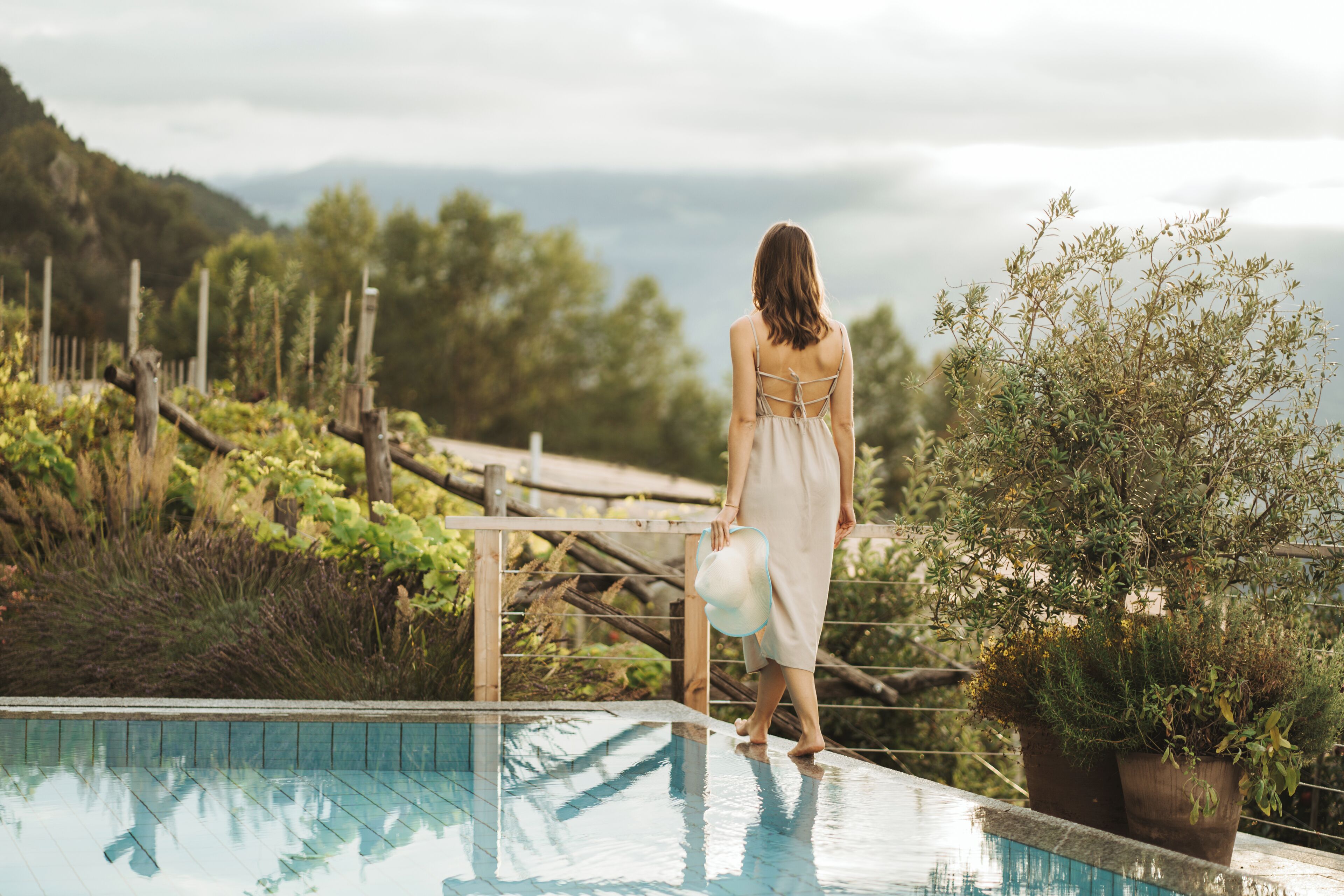 Eine Frau steht am Pool mit Blick auf bewaldetes Gebiet und Berge im Hintergrund.