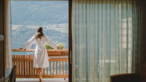 A person in a white robe standing on a balcony with a view of a mountainous landscape. - Niedermair Nature Retreat (Parcines)