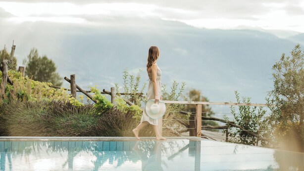 A person walking along a poolside with a mountainous backdrop. - Niedermair Nature Retreat (Parcines)
