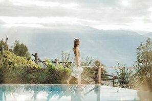 A person walking along a poolside with a mountainous backdrop. - Niedermair Nature Retreat (Parcines)