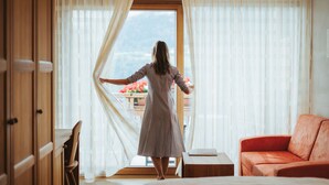 A room with a large window, a wooden wardrobe, a wooden chair, a small wooden table, and a red sofa. - Niedermair Nature Retreat (Parcines)