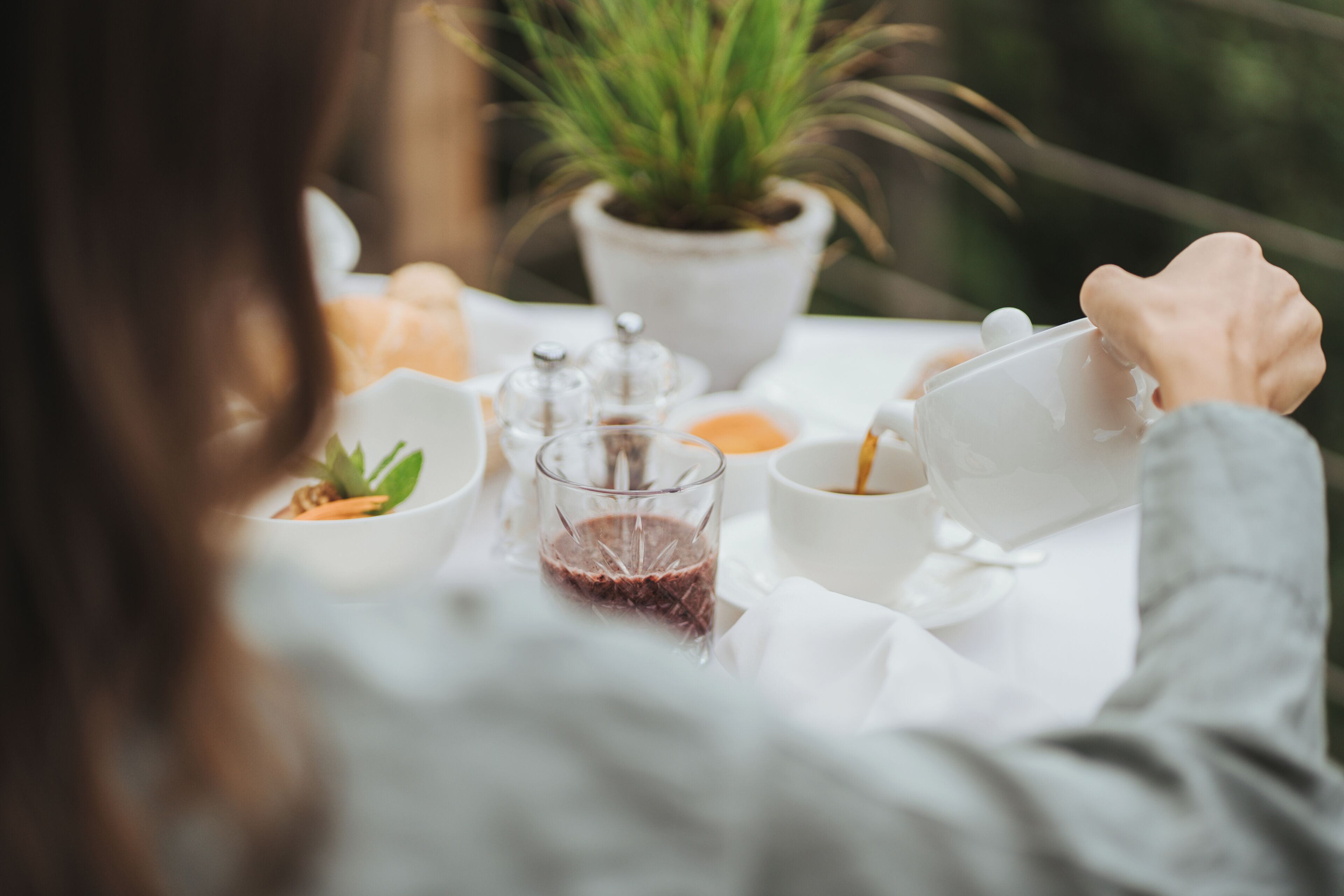 A person at a table with a potted plant, a glass of juice, and a cup with a spoon.
