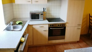 A kitchen with a microwave, stove, sink, and cabinets. - Havelapartments Gatow (Berlin)