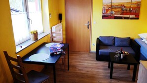 A compact living space with a wooden floor, a dining table with chairs, a sofa, and a painting on the wall. - Havelapartments Gatow (Berlin)