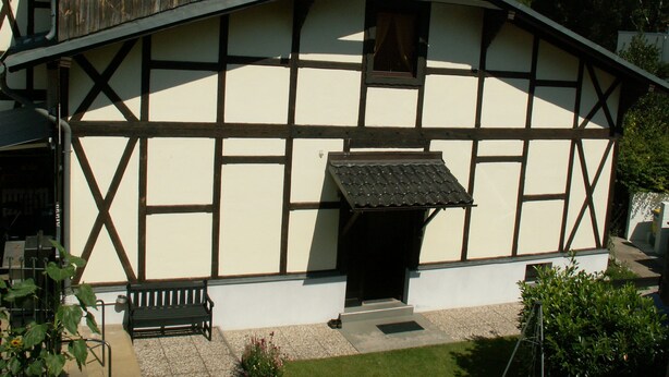A traditional half-timbered house with a sloped roof, a small porch, and a wooden bench. - Havelapartments Gatow (Berlin)