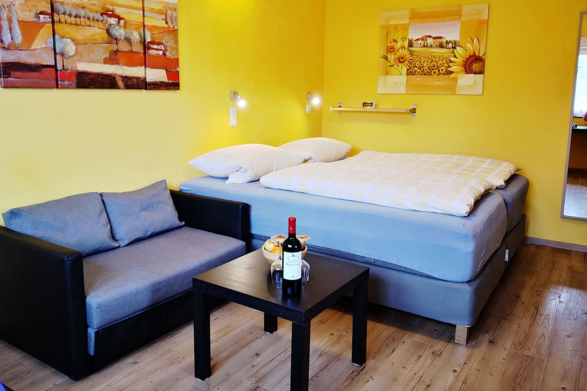 Une pièce comprenant un lit, un canapé, une table avec une bouteille et deux lampes fixées au mur.