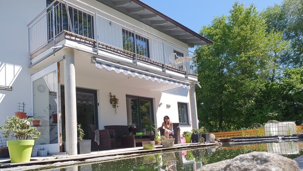 Una casa a due piani con un balcone, una piscina e piante in vaso.