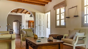 Una sala acogedora con una mesa de madera, dos sofás y una mesa de comedor. Se observa una cocina al fondo, con una ventana y una puerta que da a otra habitación.