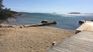 Una playa con muelle de madera, costa rocosa y mar tranquilo.