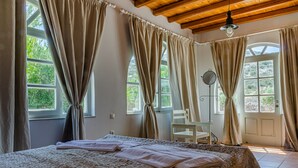 Un dormitorio con una cama grande, cortinas color beige, techo de madera y vista a zonas verdes.