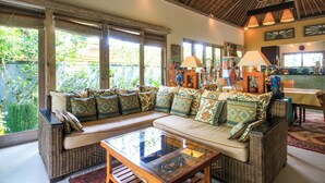 A spacious living area with a large sofa, a glass coffee table, and a dining table with chairs. - Villa Semua Suka in the Ricefields of Penestanan (Ubud)
