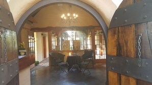 A dining area with a table and chairs, a chandelier, and a view through a window with a 'Please Wait' sign. - Since 2006 African Silhouette Offers Safe, Tranquil and Highly Recommended Stays (Benoni)
