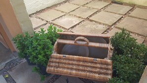 A wicker basket with a lid on a stone-paved patio next to potted plants. - Since 2006 African Silhouette Offers Safe, Tranquil and Highly Recommended Stays (Benoni)
