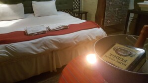 A neatly made bed with white and red linens, a small table with a book, and a chair. - Since 2006 African Silhouette Offers Safe, Tranquil and Highly Recommended Stays (Benoni)