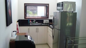 A compact kitchen with a window, a microwave, a refrigerator, and a sink. - Explore Lombok From Dream Estate (Senggigi)