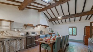 Una cocina rústica con vigas de madera a la vista, una mesa de comedor dispuesta para seis personas y un suelo de baldosas.