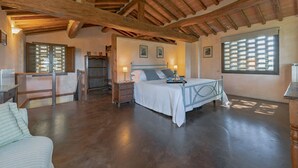 Un dormitorio amplio con techo de madera, una cama con estructura metálica, una mesita de noche con lámpara y una ventana con persianas.