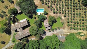 Vista aérea de una propiedad con varias construcciones, una piscina y un extenso jardín con filas de árboles.