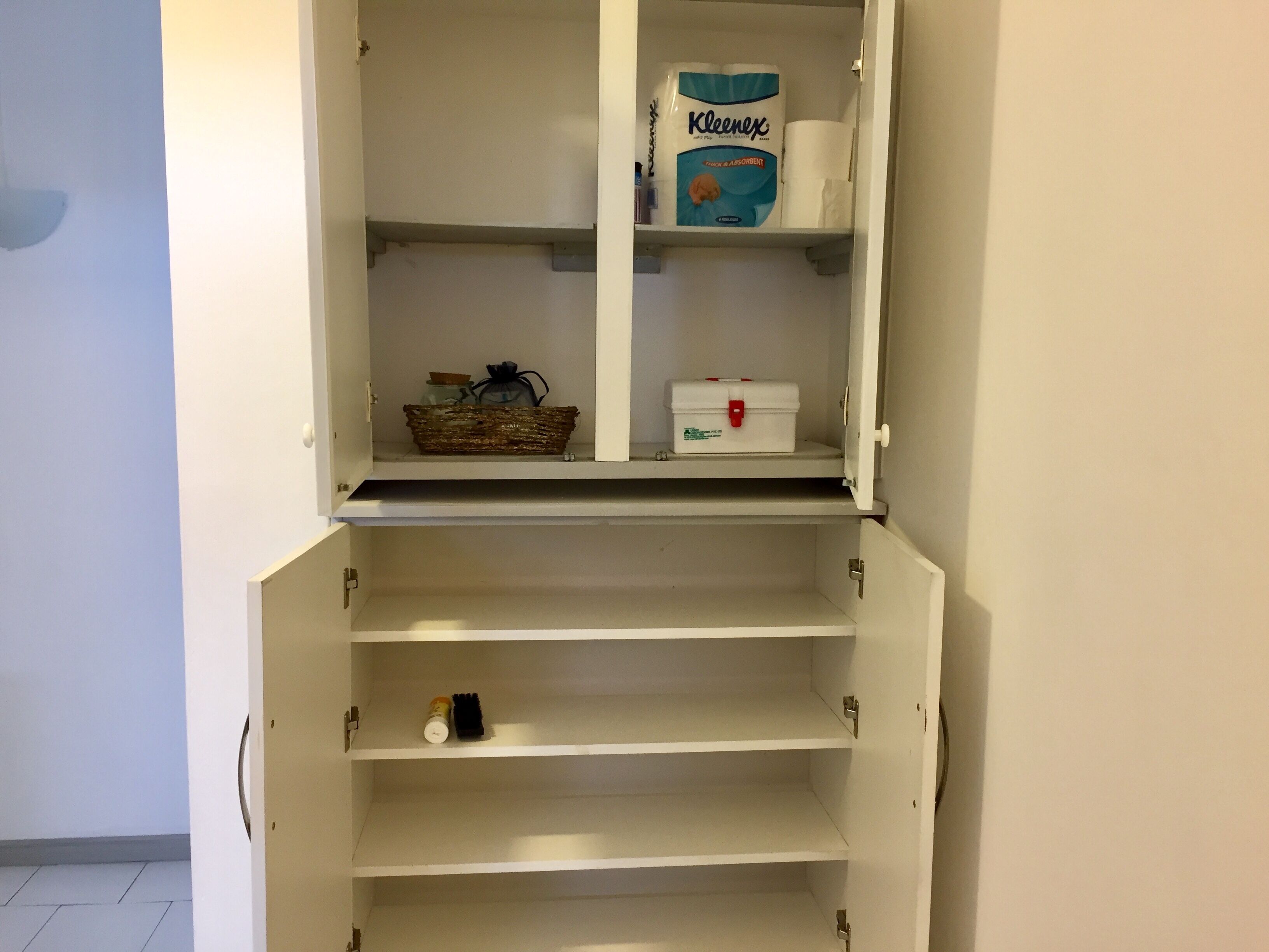 A white cabinet with shelves containing Kleenex tissues, a basket, and a small white box.