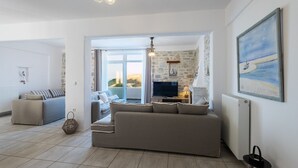 A living room with a sofa, a TV, and a stone wall. - Villa Amphitrite With Amazing sea View and Private Swimming Pool (Paros)