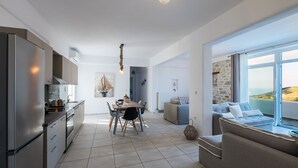A modern kitchen with a dining area, a sofa with a view, and a stone wall. - Villa Amphitrite With Amazing sea View and Private Swimming Pool (Paros)