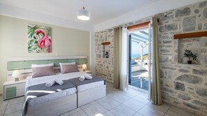 A bedroom with a bed, a nightstand, a wall painting, a stone wall, and a view through a glass door. - Villa Amphitrite With Amazing sea View and Private Swimming Pool (Paros)