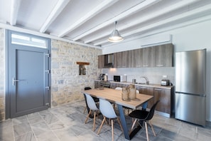 Una cocina moderna con paredes de piedra, armarios de madera, un refrigerador de acero inoxidable y una zona de comedor con mesa y sillas de madera.