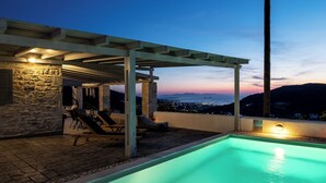 Piscina con muro de piedra y sillones de descanso bajo una pérgola, con vistas panorámicas.