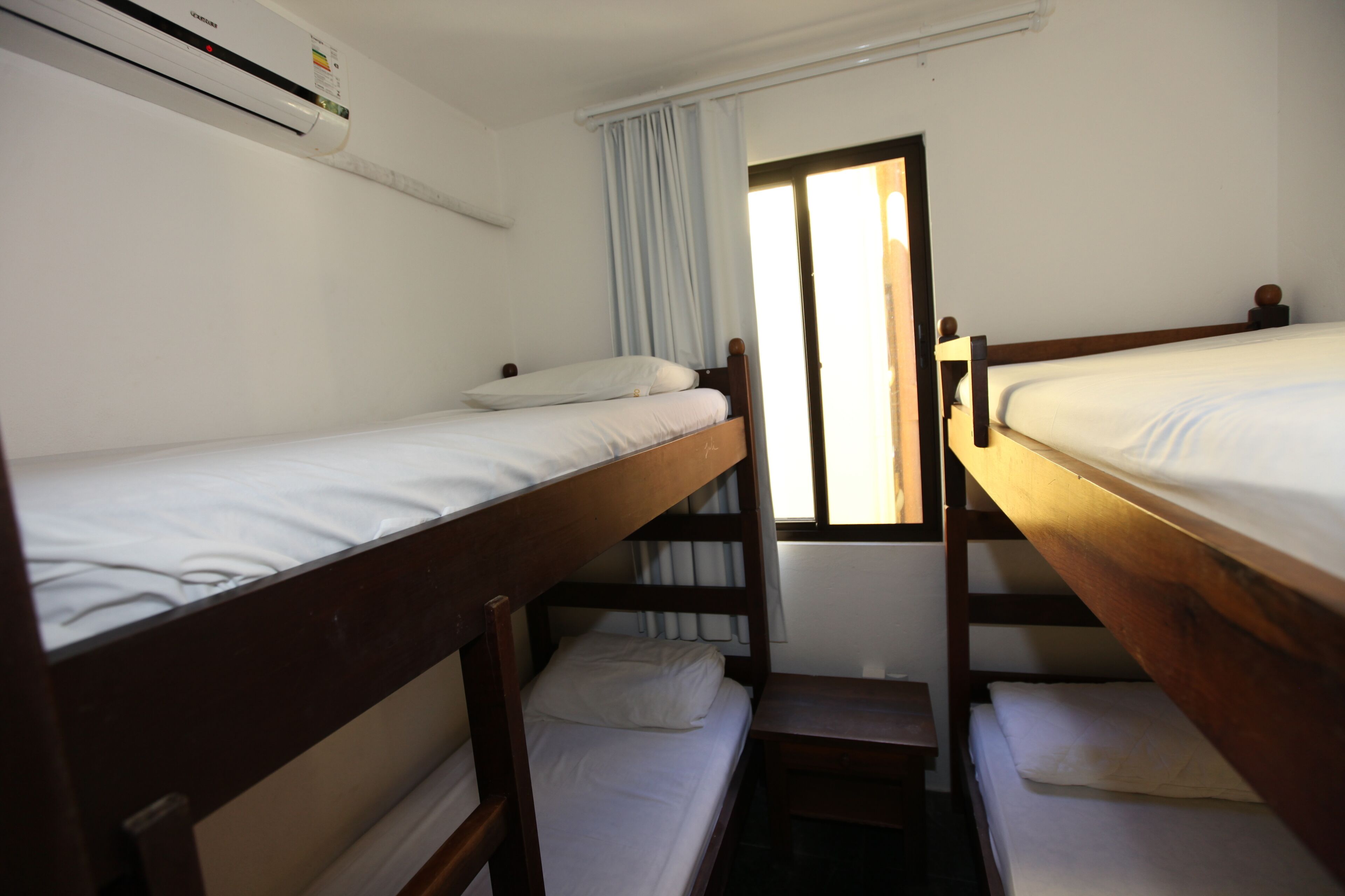 Ein Schlafsaalzimmer mit Etagenbetten, einem Vorhangfenster und einer wandmontierten Klimaanlage.
