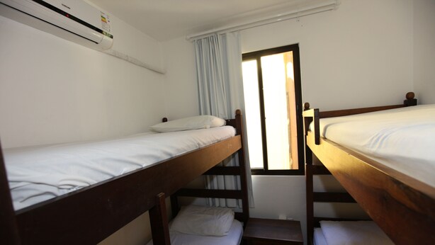 Habitación tipo dormitorio con literas, una ventana con cortinas y un aire acondicionado instalado en la pared.