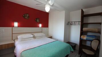 A bedroom with a bed, a nightstand, a chair, a shelf with towels, and a red wall with decorative items.