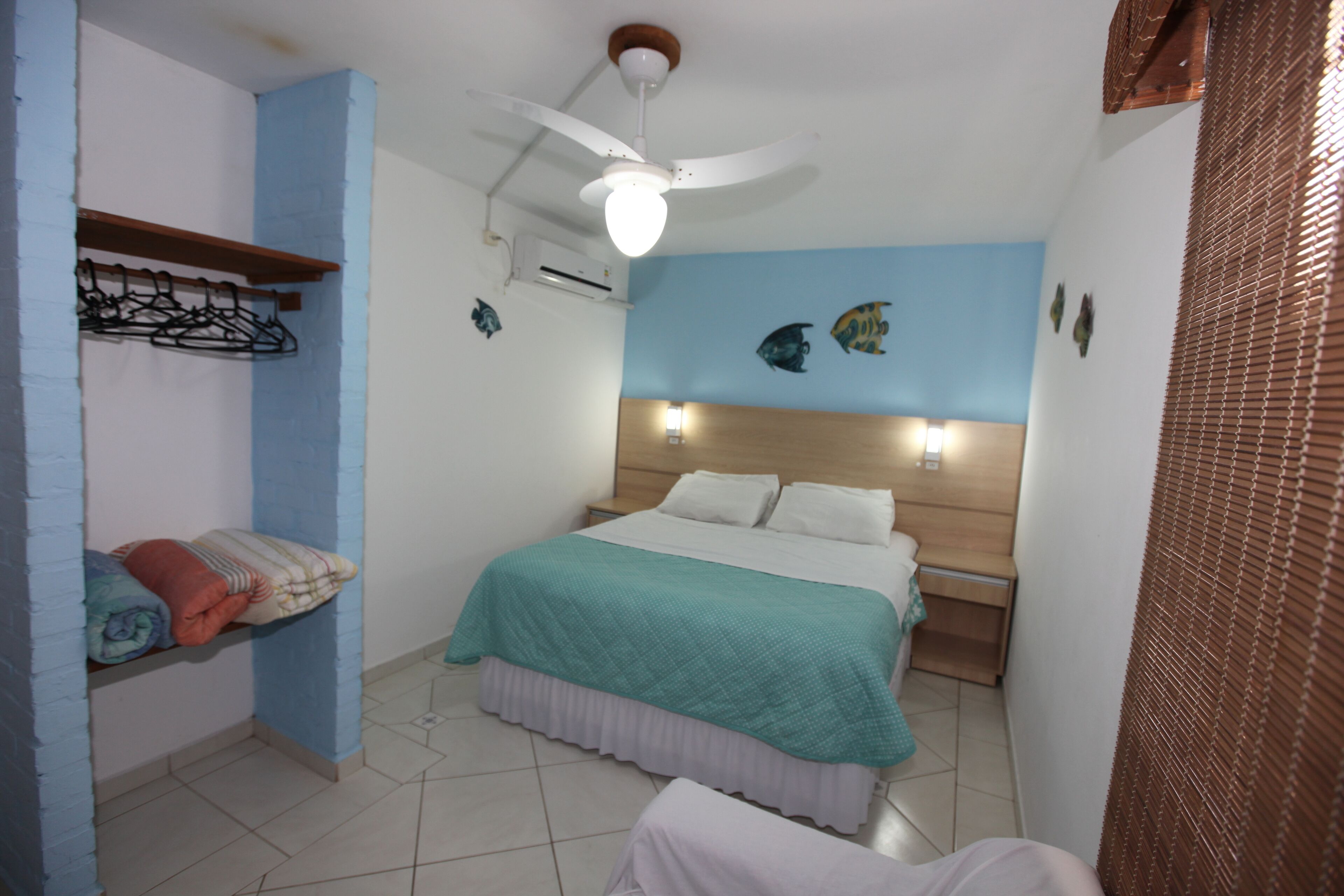 A bedroom with a bed, a ceiling fan, a wall-mounted shelf with towels, and a wall with fish decorations.